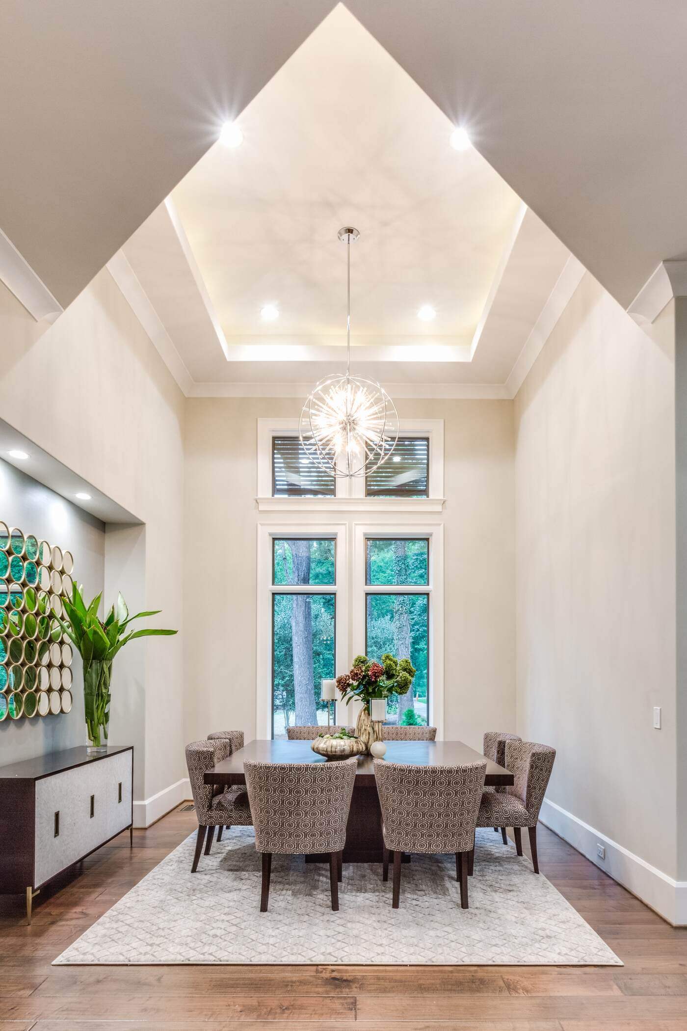 Elegant dining area in Greensboro custom home by Wolfe Homes, featuring modern chandelier lighting and large windows