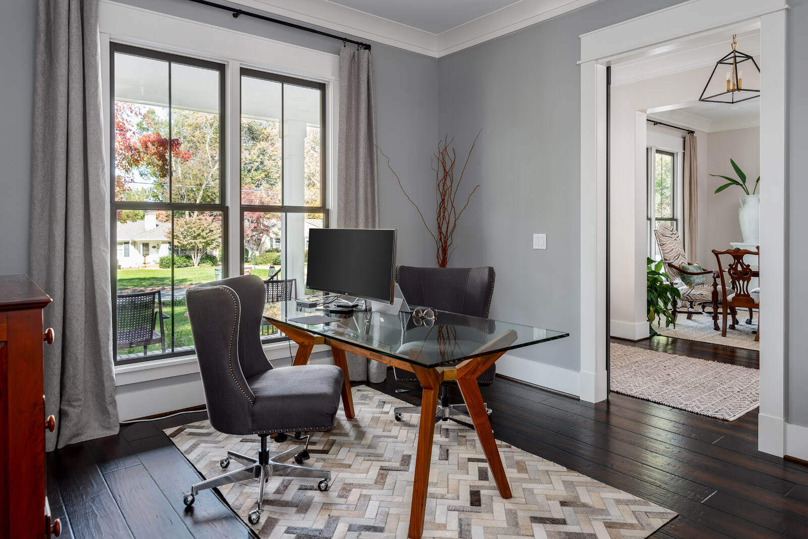 Modern home office with a glass desk and large windows by Wolfe Homes in Greensboro, NC